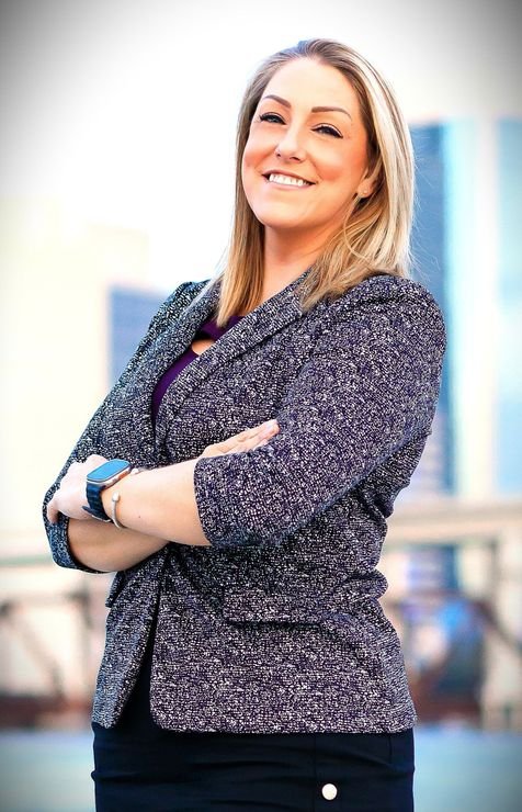 A woman wearing a purple shirt and a black jacket is smiling for the camera.